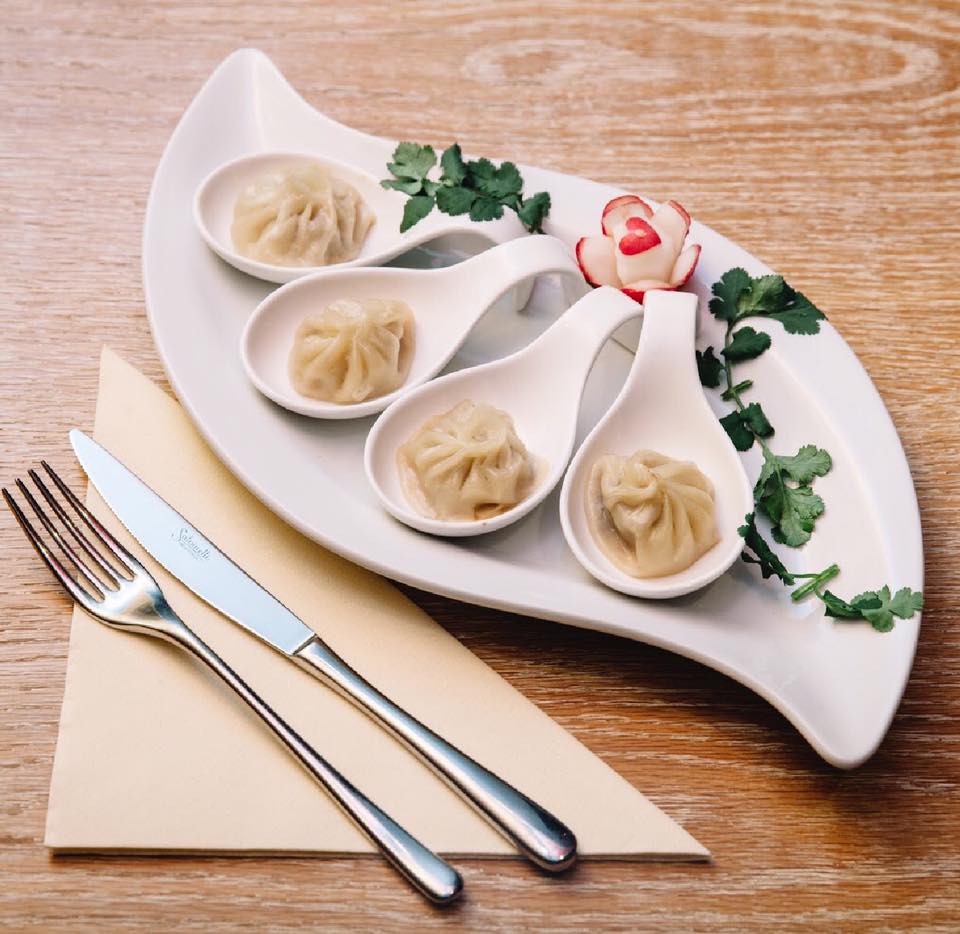 Ravioli al vapore serviti su cucchiai bianchi con erbe fresche
